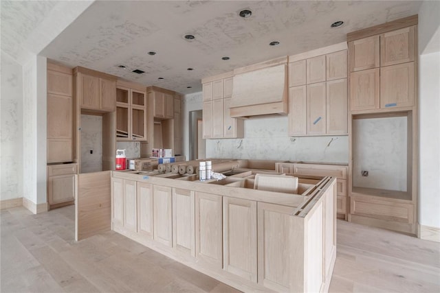 kitchen with light brown cabinets, custom range hood, light hardwood / wood-style floors, and a kitchen island