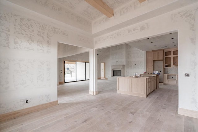 kitchen with light brown cabinetry, beam ceiling, and a towering ceiling