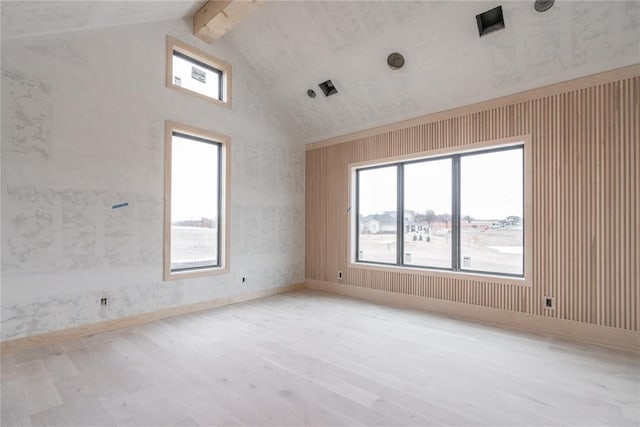 spare room with beam ceiling, high vaulted ceiling, a wealth of natural light, and light hardwood / wood-style floors