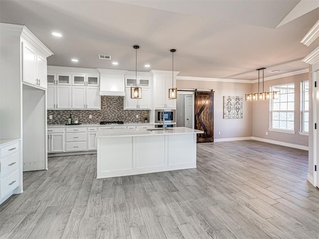 kitchen featuring white cabinets, a barn door, decorative light fixtures, and an island with sink