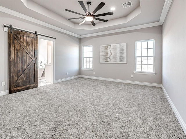 carpeted empty room with a barn door, a tray ceiling, ceiling fan, and crown molding