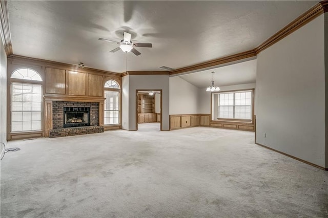 unfurnished living room featuring carpet flooring, ceiling fan with notable chandelier, crown molding, and a brick fireplace