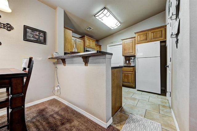 kitchen featuring lofted ceiling, a kitchen breakfast bar, light tile patterned floors, white fridge, and kitchen peninsula