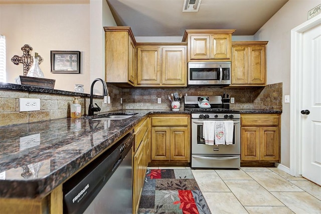 kitchen featuring backsplash, sink, dark stone countertops, light tile patterned floors, and appliances with stainless steel finishes