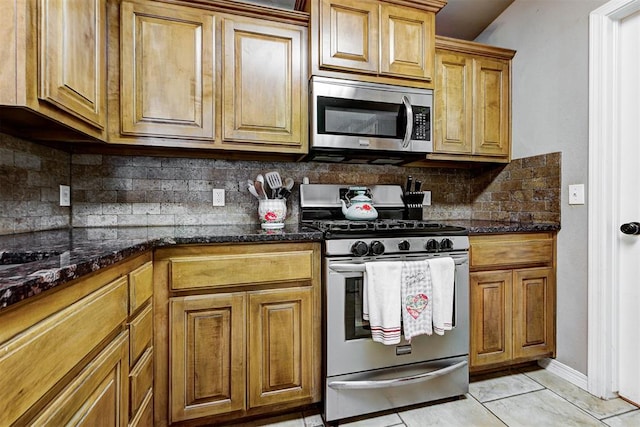 kitchen featuring light tile patterned flooring, dark stone countertops, stainless steel appliances, and tasteful backsplash