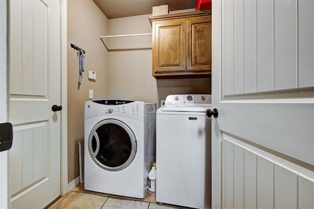 clothes washing area with cabinets, washing machine and dryer, and light tile patterned floors