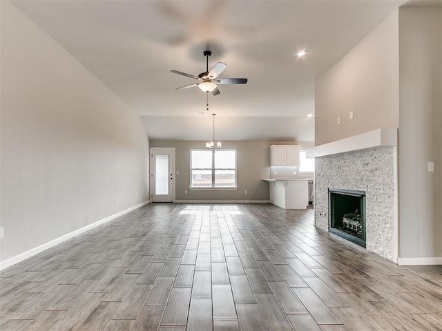 unfurnished living room with ceiling fan with notable chandelier, light hardwood / wood-style floors, and a fireplace