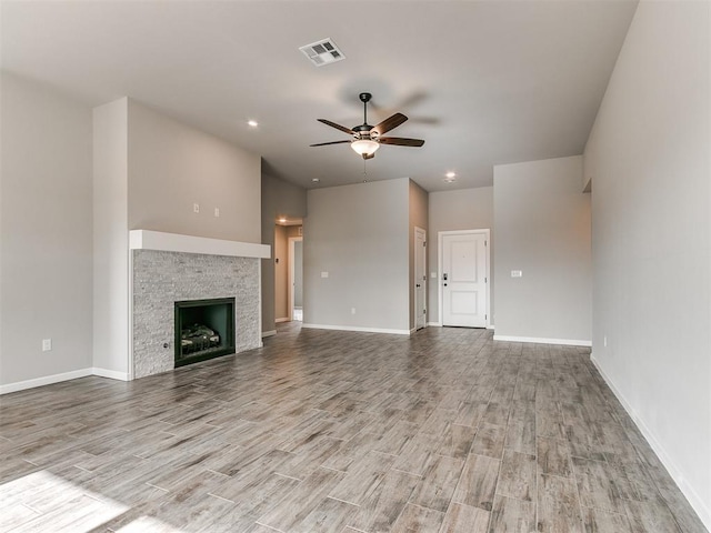 unfurnished living room with light hardwood / wood-style flooring, a stone fireplace, and ceiling fan