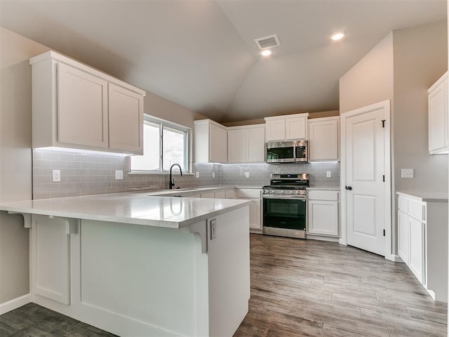 kitchen featuring kitchen peninsula, white cabinetry, lofted ceiling, and stainless steel appliances