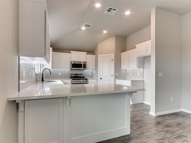 kitchen featuring kitchen peninsula, appliances with stainless steel finishes, wood-type flooring, white cabinets, and lofted ceiling