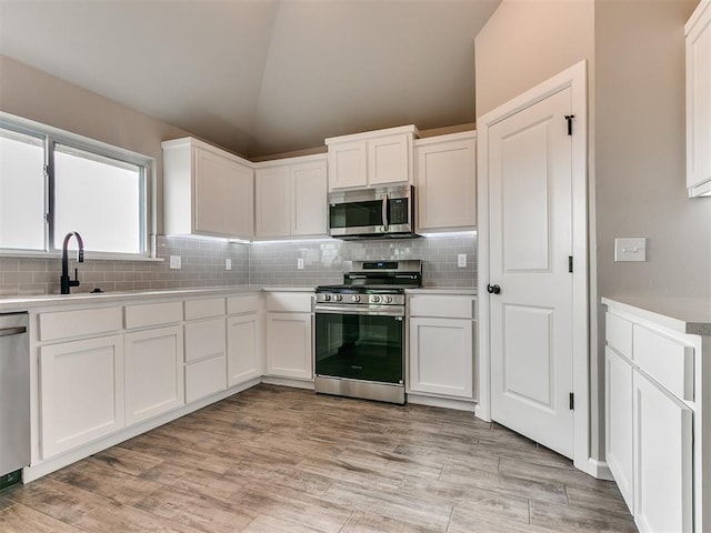 kitchen featuring light hardwood / wood-style floors, white cabinetry, stainless steel appliances, and vaulted ceiling