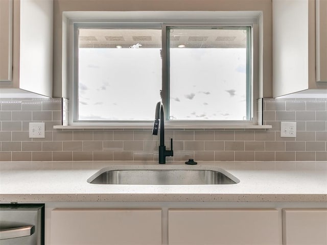 kitchen with tasteful backsplash, light stone counters, plenty of natural light, and sink