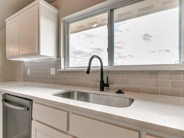 kitchen with light stone countertops, dishwasher, sink, white cabinetry, and tasteful backsplash