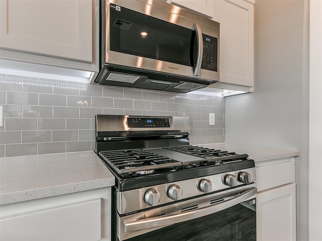 kitchen with white cabinets, decorative backsplash, light stone counters, and appliances with stainless steel finishes