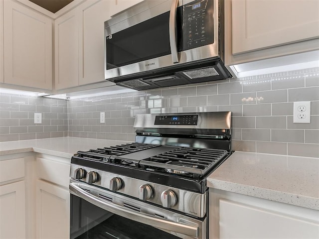 kitchen featuring backsplash, light stone counters, white cabinets, and appliances with stainless steel finishes