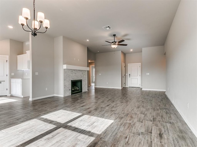 unfurnished living room with ceiling fan with notable chandelier, a stone fireplace, and light wood-type flooring