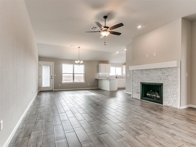 unfurnished living room with sink, a fireplace, ceiling fan with notable chandelier, and light wood-type flooring