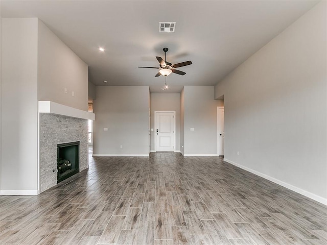 unfurnished living room with hardwood / wood-style flooring, ceiling fan, and a stone fireplace