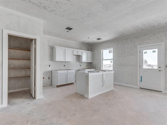 kitchen with a center island, light countertops, visible vents, white cabinetry, and unfinished concrete floors