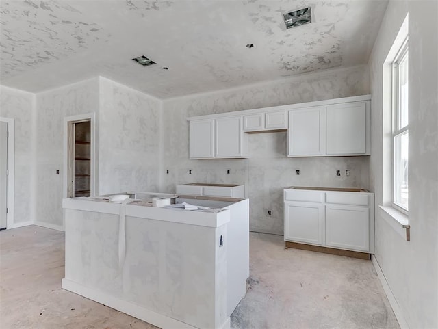 kitchen featuring concrete flooring, a kitchen island, visible vents, white cabinetry, and baseboards