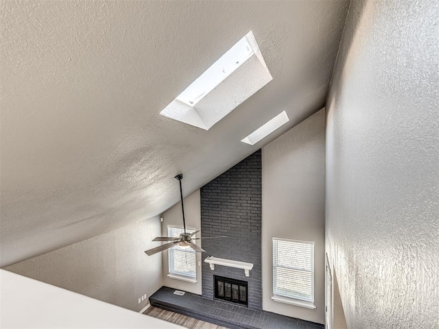 unfurnished living room with a fireplace, a healthy amount of sunlight, lofted ceiling with skylight, and a textured ceiling