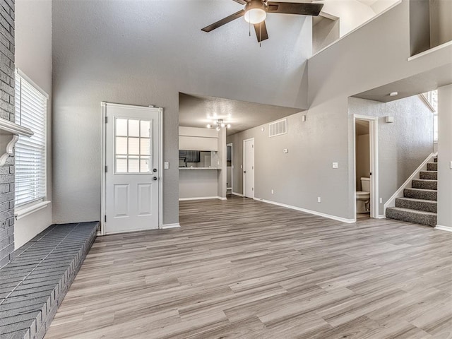 unfurnished living room featuring ceiling fan, light hardwood / wood-style floors, and a high ceiling