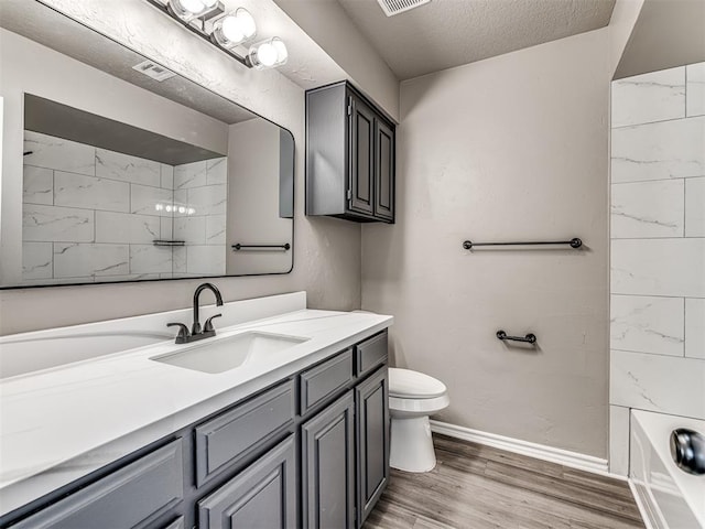 full bathroom featuring vanity, tiled shower / bath, hardwood / wood-style flooring, toilet, and a textured ceiling