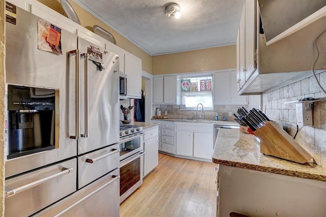 kitchen with backsplash, light stone counters, stainless steel appliances, sink, and white cabinets