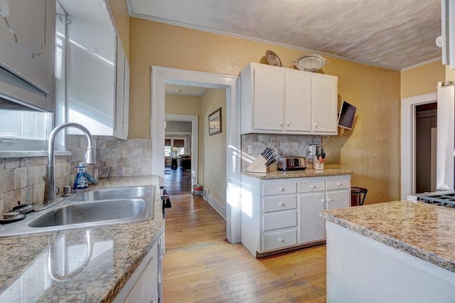 kitchen featuring sink, decorative backsplash, light stone countertops, light wood-type flooring, and white cabinetry