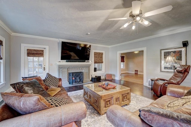 living room featuring ceiling fan, light wood-type flooring, a textured ceiling, a fireplace, and ornamental molding