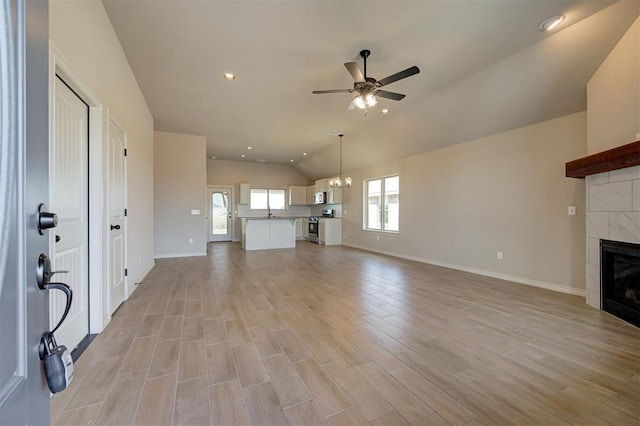 unfurnished living room featuring a fireplace, ceiling fan with notable chandelier, lofted ceiling, and light hardwood / wood-style flooring