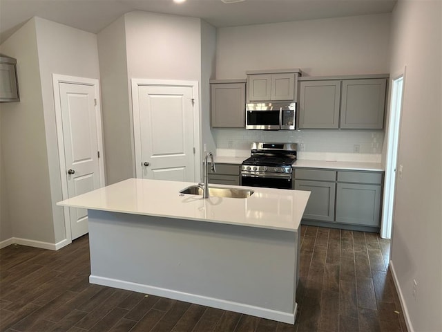 kitchen featuring gray cabinetry, sink, a kitchen island with sink, stainless steel appliances, and decorative backsplash