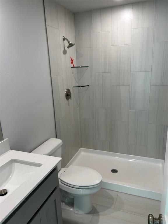 bathroom with tiled shower, vanity, and toilet