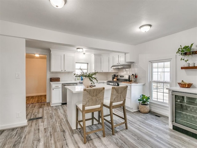 kitchen featuring backsplash, stainless steel appliances, beverage cooler, light hardwood / wood-style flooring, and white cabinetry