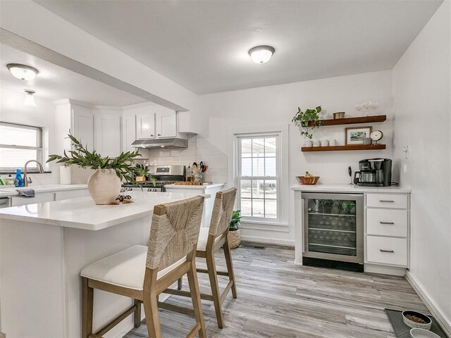 bar with gas stove, white cabinetry, wine cooler, decorative backsplash, and light wood-type flooring