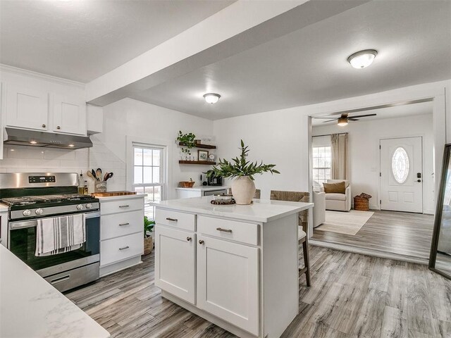 kitchen featuring stainless steel range with gas cooktop, light hardwood / wood-style flooring, white cabinets, and a kitchen island