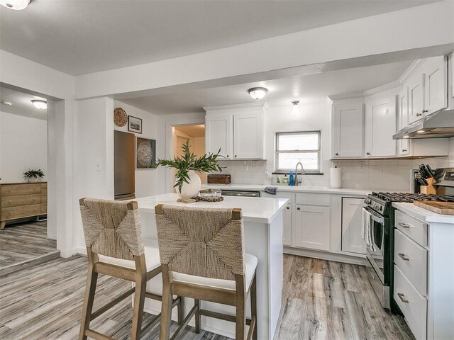 kitchen with white cabinetry, tasteful backsplash, light hardwood / wood-style floors, a breakfast bar area, and stainless steel range with gas stovetop