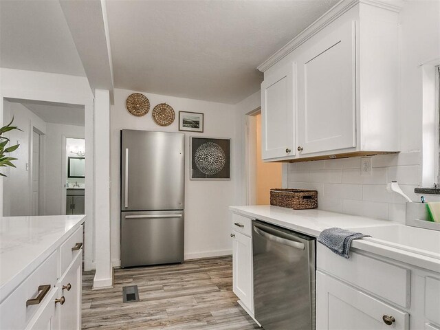 kitchen with sink, stainless steel appliances, tasteful backsplash, white cabinets, and light wood-type flooring