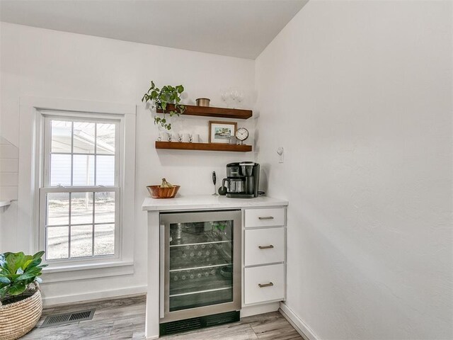 bar with beverage cooler and light hardwood / wood-style flooring