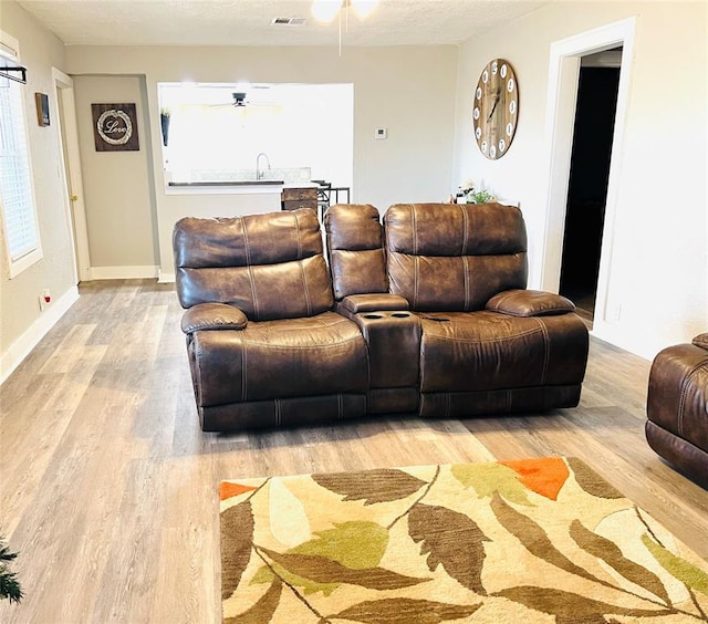 living room with ceiling fan, light hardwood / wood-style floors, and a textured ceiling