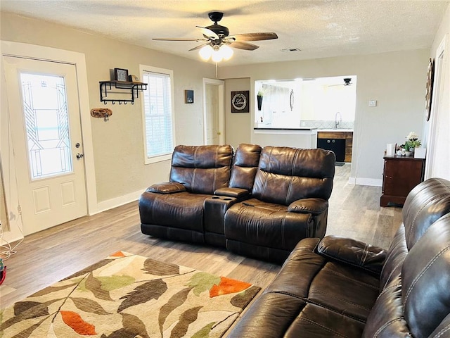 living room featuring ceiling fan, sink, a textured ceiling, and light wood-type flooring