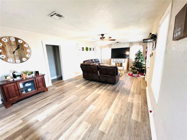 living room featuring a textured ceiling, light wood-type flooring, and ceiling fan