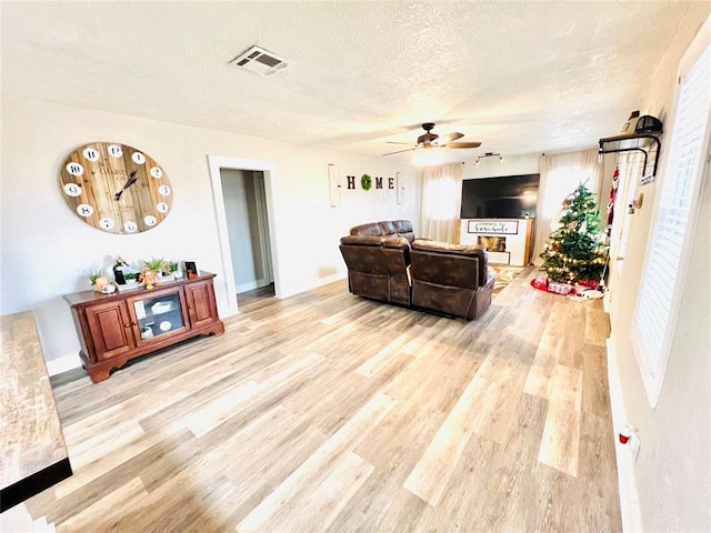 living room featuring ceiling fan, light wood-type flooring, and a textured ceiling