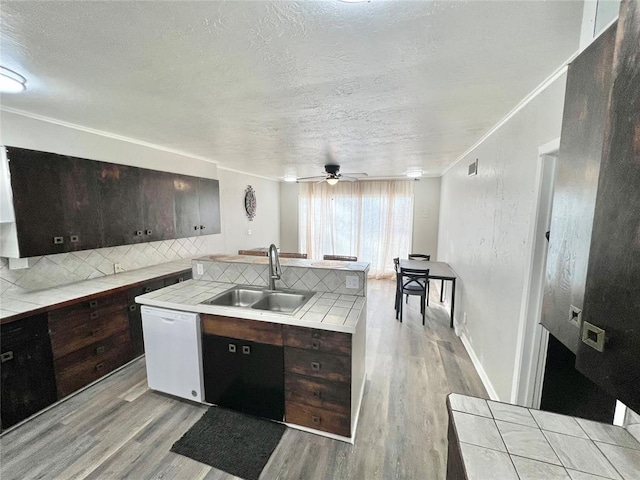 kitchen with dark brown cabinets, sink, tile countertops, dishwasher, and light hardwood / wood-style floors