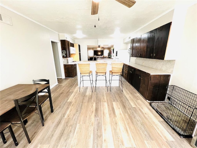 kitchen featuring white refrigerator, kitchen peninsula, a breakfast bar area, dark brown cabinets, and light wood-type flooring