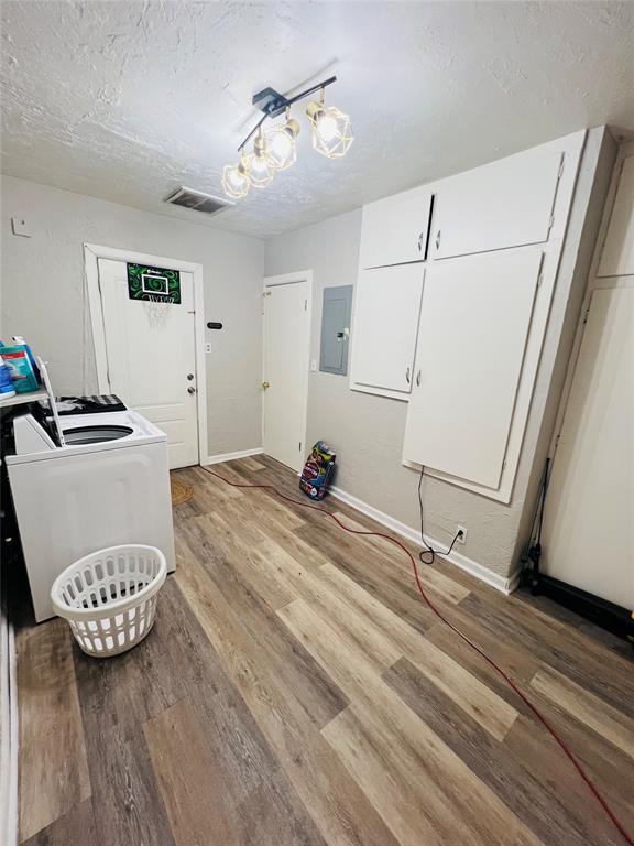 laundry room featuring washer / clothes dryer, electric panel, a textured ceiling, and light wood-type flooring