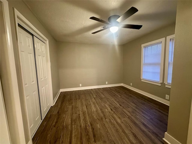 unfurnished bedroom with ceiling fan, a closet, dark wood-type flooring, and a textured ceiling