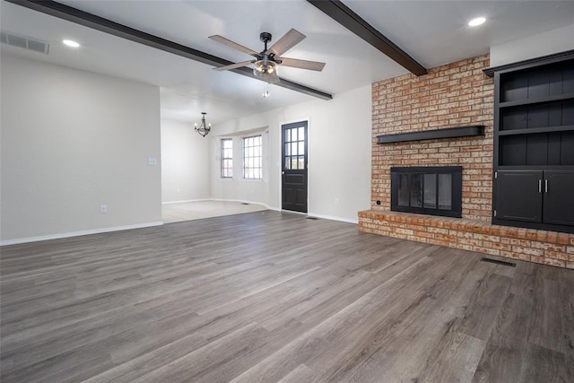 unfurnished living room featuring a brick fireplace, beamed ceiling, ceiling fan with notable chandelier, and hardwood / wood-style flooring