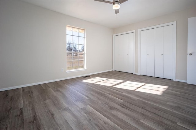 unfurnished bedroom with dark hardwood / wood-style flooring, two closets, and ceiling fan