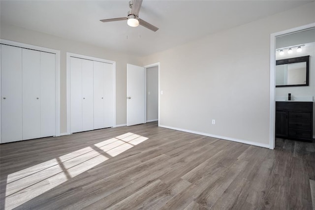 unfurnished bedroom featuring hardwood / wood-style floors, ensuite bathroom, ceiling fan, and multiple closets